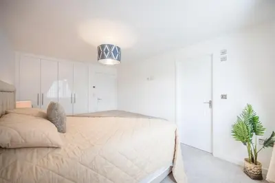 a white bedroom with a bed and a potted plant at A Superb 5BR House near SZC in Leiston