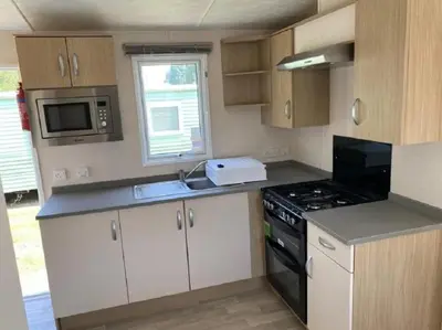 a small kitchen with a stove and a microwave at Caravan With Front Decking At Coopers Beach Holiday Park Ref 49080Pa in East Mersea