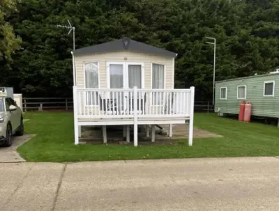 a small white house with a porch and a car at Caravan With Front Decking At Coopers Beach Holiday Park Ref 49080Pa in East Mersea