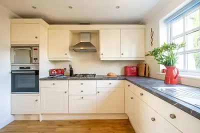 a white kitchen with white cabinets and a window at 7 Sanctuary Court - sleeps 12 - Thorpeness - Aldeburgh Coastal Cottages - Close to the Beach, Golf and the Country Club in Thorpeness