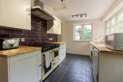 a kitchen with white cabinets and black tiles on the wall at The Manor Dairy in Sandy