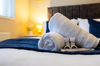 a rolled up towel and money on a bed at Modern Comfort, Free Parking, Netflix & Disney plus in every Bedroom and Living Room in Shephall