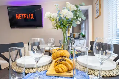 a table with a vase of flowers and wine glasses at Modern Comfort, Free Parking, Netflix & Disney plus in every Bedroom and Living Room in Shephall