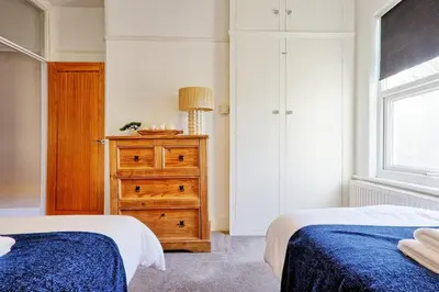 a bedroom with two beds and a dresser and a window at Cosy 2 Bedroom Flat Near Westcliff On Sea Beach & Hamlet Court Road in Southend-on-Sea