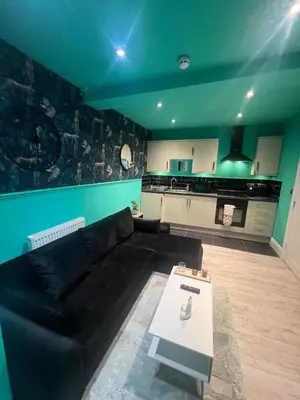 a living room with a black couch and a kitchen at The Emerald Aura Stay By Cambridge Central Station in Cambridge