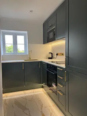 a kitchen with dark green cabinets and a window at Lavish The White Apartment in Bury Saint Edmunds