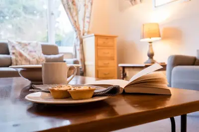 an open book on a table with muffins and a cup of coffee at 1 Hall Farm Cottage, Aldeburgh in Aldeburgh