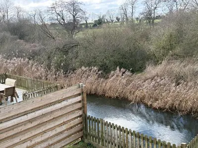 a wooden fence next to a river with a bench at Owls Nest in Larling