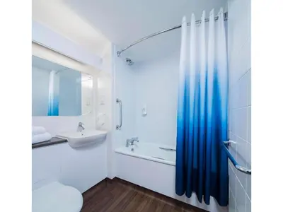 a white bathroom with a blue shower curtain and a sink at Travelodge Harlow in Harlow