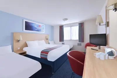 a hotel room with two beds and a chair at Travelodge Colchester Feering in Feering