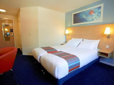 a hotel room with a large bed and a red chair at Travelodge Ipswich Capel St Mary in Capel Saint Mary