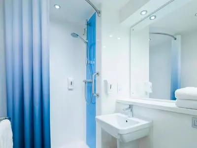 a bathroom with a sink and a shower with a mirror at Travelodge Cambridge Swavesey in Bar Hill