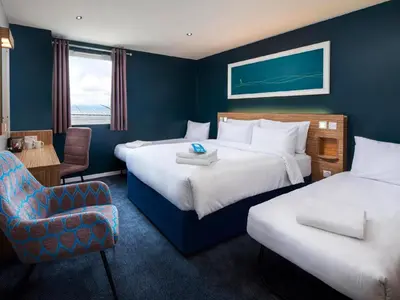 a hotel room with two beds and a chair at Travelodge Cambridge Swavesey in Bar Hill