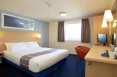 a hotel room with a bed and a desk with a computer at Travelodge Cambridge Swavesey in Bar Hill
