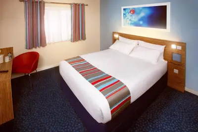 a hotel room with a bed and a red chair at Travelodge Huntingdon Fenstanton in Fenstanton