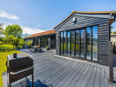 a wooden deck with a grill and a building at Essex Barn House - Uk48354 in Romford