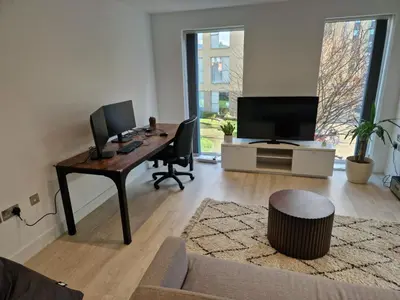 a living room with a desk with a computer and a tv at Bright Corner Apartment by Cambridge Station with Free Allocated Underground Parking & Flexible Beds in Cambridge