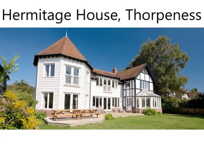 a large white house with a bench in front of it at Hermitage House, Thorpeness - sleeps 12 - Large Thorpeness house on the banks of Thorpness Meare - a boating lake - Close to Thorpeness beach, Golf Club and Thorpeness Country Club - Aldeburgh Coastal Cottages in Thorpeness