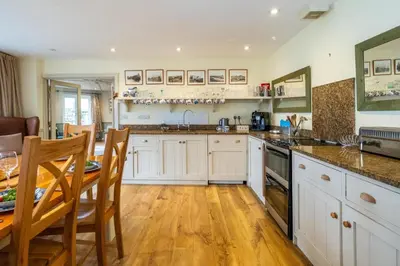 a kitchen with white cabinets and a table and a dining room at Hermitage House, Thorpeness - sleeps 12 - Large Thorpeness house on the banks of Thorpness Meare - a boating lake - Close to Thorpeness beach, Golf Club and Thorpeness Country Club - Aldeburgh Coastal Cottages in Thorpeness