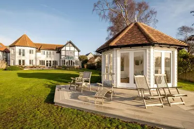 a gazebo with chairs on a deck in front of a house at Hermitage House, Thorpeness - sleeps 12 - Large Thorpeness house on the banks of Thorpness Meare - a boating lake - Close to Thorpeness beach, Golf Club and Thorpeness Country Club - Aldeburgh Coastal Cottages in Thorpeness