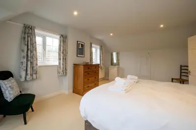 a bedroom with a large white bed and a chair at Heronsmead, sleeps 8 - Large Thorpeness house on the banks of Thorpness Meare - a boating lake - Close to Thorpeness beach, Golf Club and Thorpeness Country Club - Aldeburgh Coastal Cottages in Thorpeness