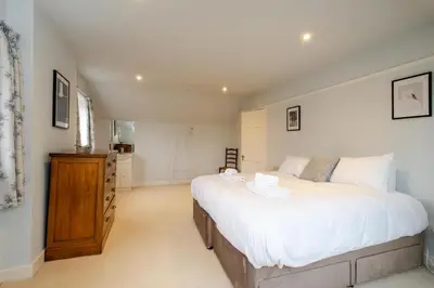a bedroom with a large white bed and a wooden dresser at Heronsmead, sleeps 8 - Large Thorpeness house on the banks of Thorpness Meare - a boating lake - Close to Thorpeness beach, Golf Club and Thorpeness Country Club - Aldeburgh Coastal Cottages in Thorpeness