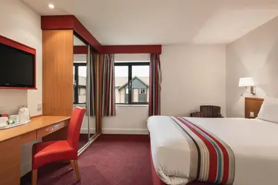 a hotel room with a bed and a desk and a television at Ramada Cambridge in Cambridge