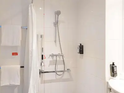 a white bathroom with a shower and a sink at ibis Cambridge Central Station in Cambridge