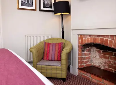 a yellow chair with a pillow sitting next to a fireplace at The Bushel by Greene King Inns in Bury Saint Edmunds