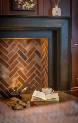 a book and a cup of coffee next to a fireplace at Clayton Hotel Cambridge in Cambridge