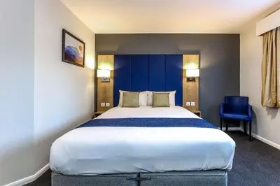 a large bed in a hotel room with a blue wall at Days Inn London Stansted Airport in Stansted Mountfitchet
