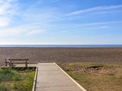 a wooden boardwalk leading to a bench on a beach at 7 The Uplands in Thorpeness