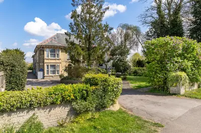 a house with a stone wall and bushes at Shelford Lodge in Cambridge