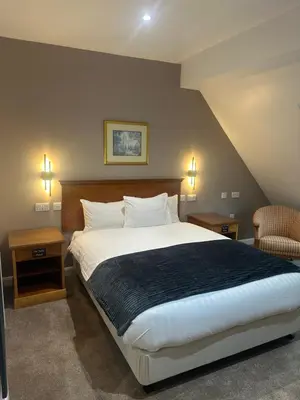 a bedroom with a large bed and two tables and a chair at Desalis Hotel London Stansted in Elsenham