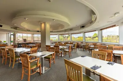 a dining room with tables and chairs and windows at Holiday Inn Basildon by IHG in Basildon