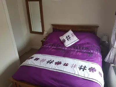 a bed with a purple comforter and a pillow at Flint Cottage in Brandon