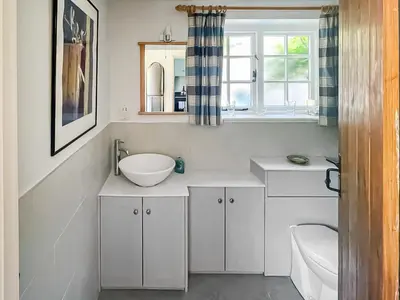 a bathroom with white cabinets and a sink and a window at Thatched Cottage in Saxmundham