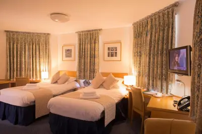 a hotel room with two beds and a desk at Madingley Hall in Cambridge
