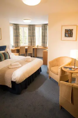 a hotel room with a bed and a chair and a desk at Madingley Hall in Cambridge