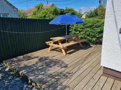 a wooden picnic table with an umbrella on a deck at Sandy Cottage in Clacton-on-Sea