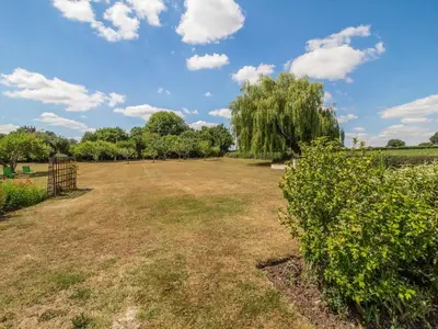a large grass field with a fence and trees at Norbank Cottage in Bressingham