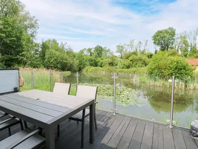 a wooden deck with a table and chairs next to a lake at Dragonfly Lodge in Yaxham
