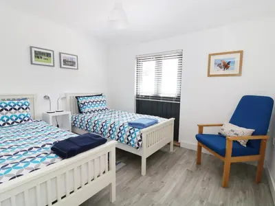 a bedroom with two beds and a blue chair at Whitehands Farm Barn in Old Buckenham