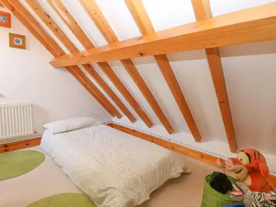 a attic bedroom with a bed and wooden beams at Stable Cottage in West Bradenham