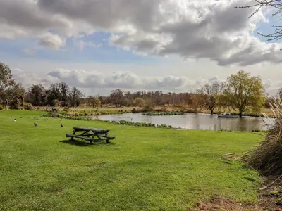 a picnic table in a field next to a river at Hayloft Cottage in Little Glenham