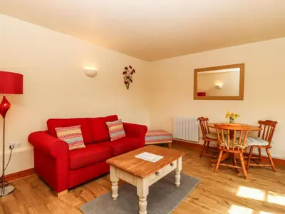 a living room with a red couch and a table at Poppy Cottage in Little Glenham