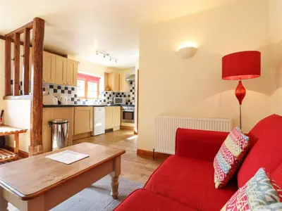 a living room with a red couch and a table at Poppy Cottage in Little Glenham