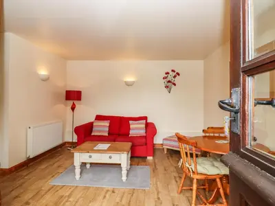 a living room with a red couch and a table at Poppy Cottage in Little Glenham