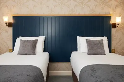 two beds in a room with a blue headboard at Bull Hotel by Greene King Inns in Long Melford