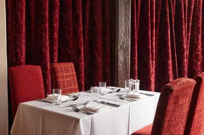 a table in a restaurant with red curtains at Bull Hotel by Greene King Inns in Long Melford